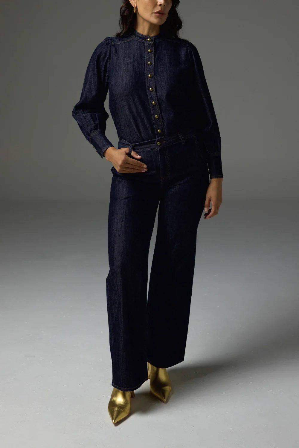 Woman wearing a dark blue outfit with gold shoes on a gray background