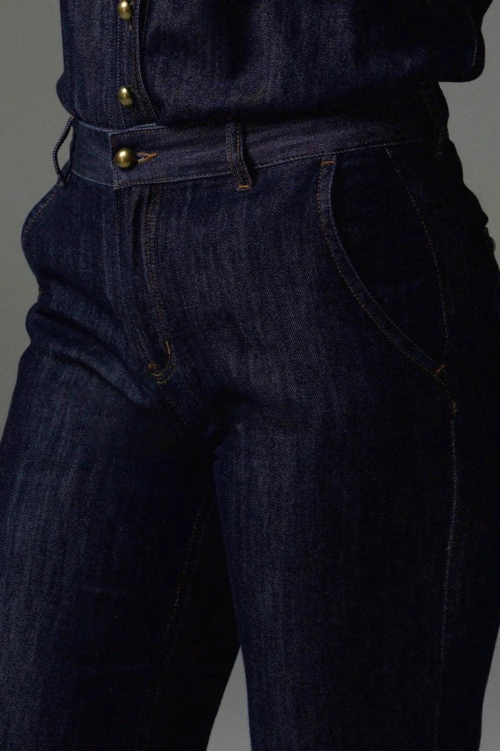 Dark blue denim jeans with gold buttons on a gray background